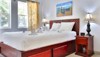 A bright bedroom with a wooden bed, white bedding, two bedside lamps, purple flowers, and ocean-themed wall art.