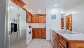 Bright kitchen with wood cabinets, white appliances, counters, and a sink in a clean, modern room.