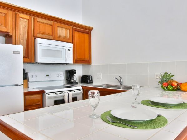A bright kitchen with wooden cabinets, microwave and stove, a sink, and a dining table set with plates, glasses, and fruit.