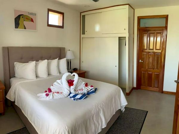 A tidy hotel bedroom with a king bed, heart-shaped towel, rose petals, and wooden doors.