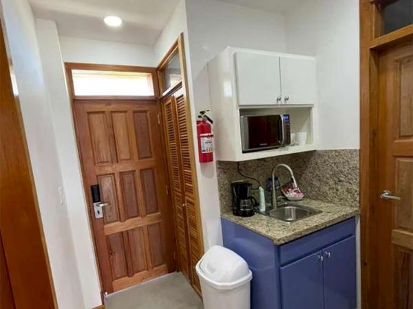 Small bathroom with blue vanity and granite counter, sink, recessed microwave, toilet, wooden doors, and a fire extinguisher.
