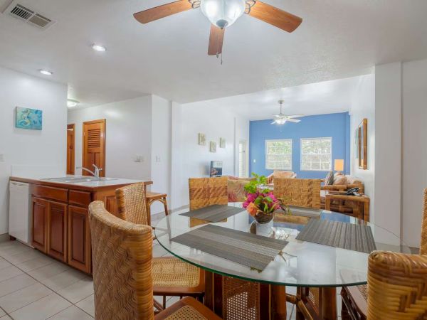 A bright dining room with a glass-top table, woven chairs, floral centerpiece, tiled floor, and ceiling fans.