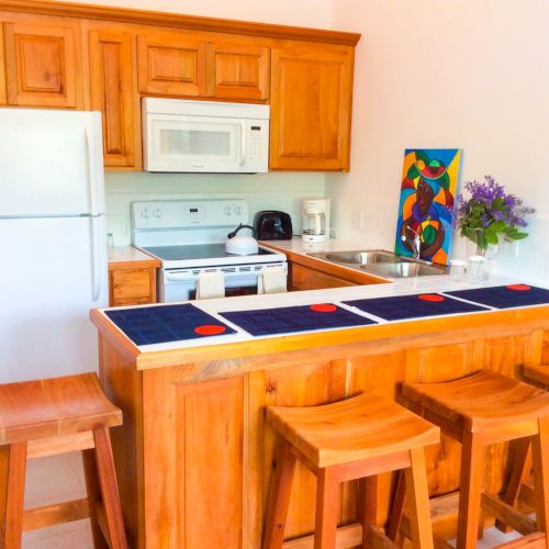 A bright kitchen with wooden cabinets, a stove/oven, microwave, sink, refrigerator, and a colorful painting beside fresh flowers.