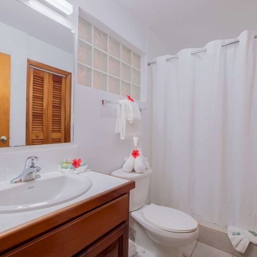 Bright bathroom with a sink vanity, toilet, white shower curtain, and rolled towels for a clean, cozy look.