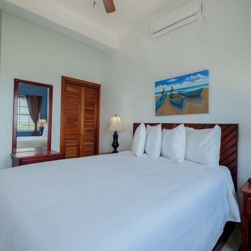 A bright hotel bedroom with a neatly made king-size bed, nightstands, lamps, and framed wall art.