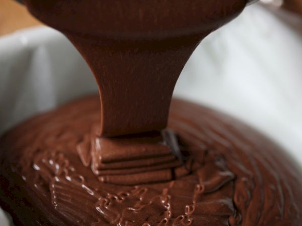 A close-up of chocolate being poured or spread over a dessert base, with glossy cocoa smearing and dripping.